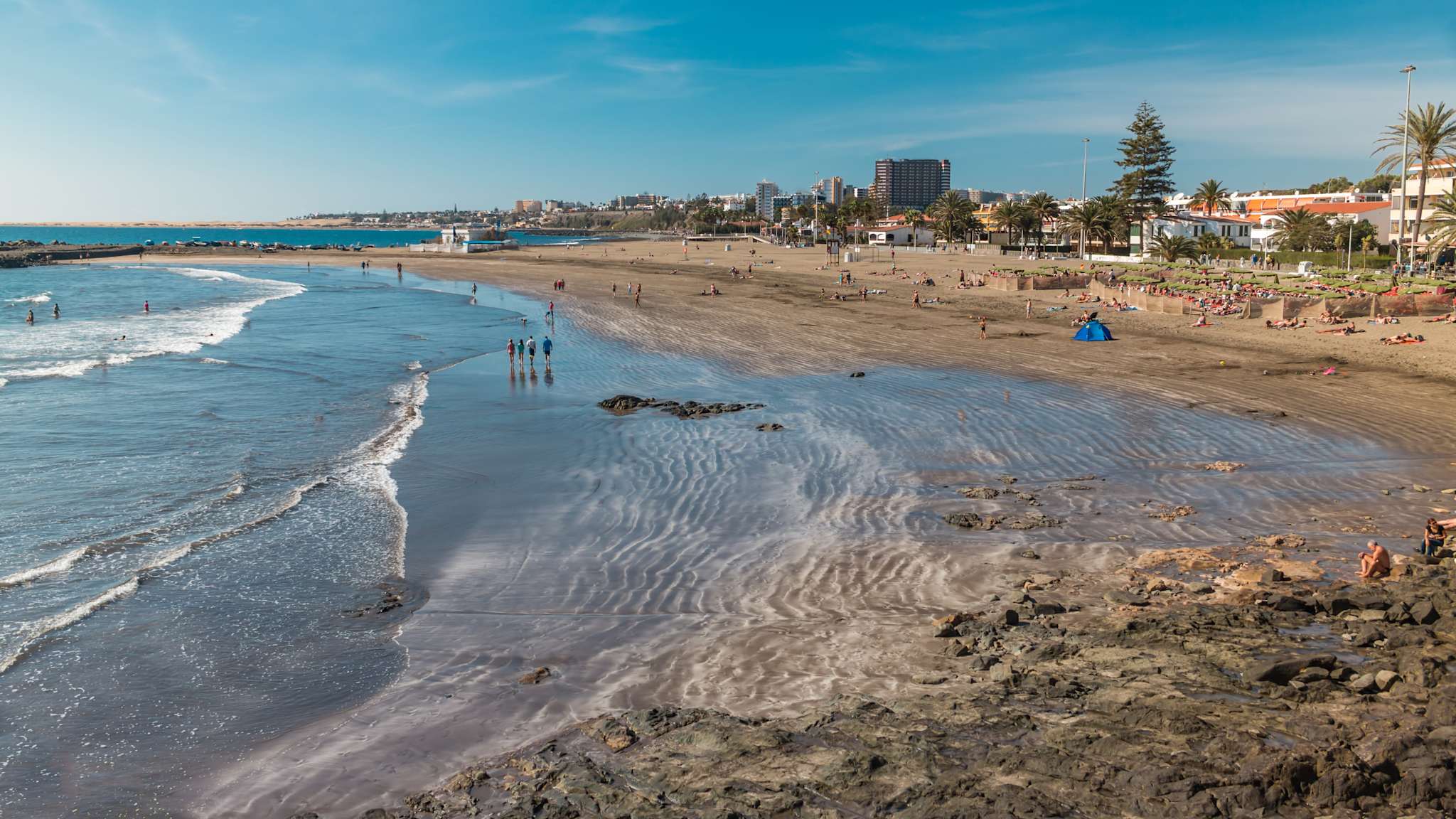 Ein weiter Strand mit hohen Gebäude im Hintergrund unter blauem Himmel